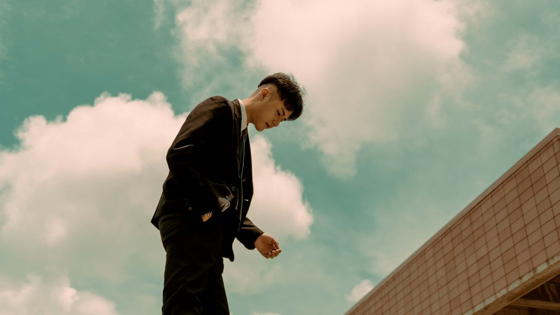 A young man wearing a modern dark suit jacket and trousers looking down, perfect for illustrating style adjustments and common suit mistakes to avoid in Orem.