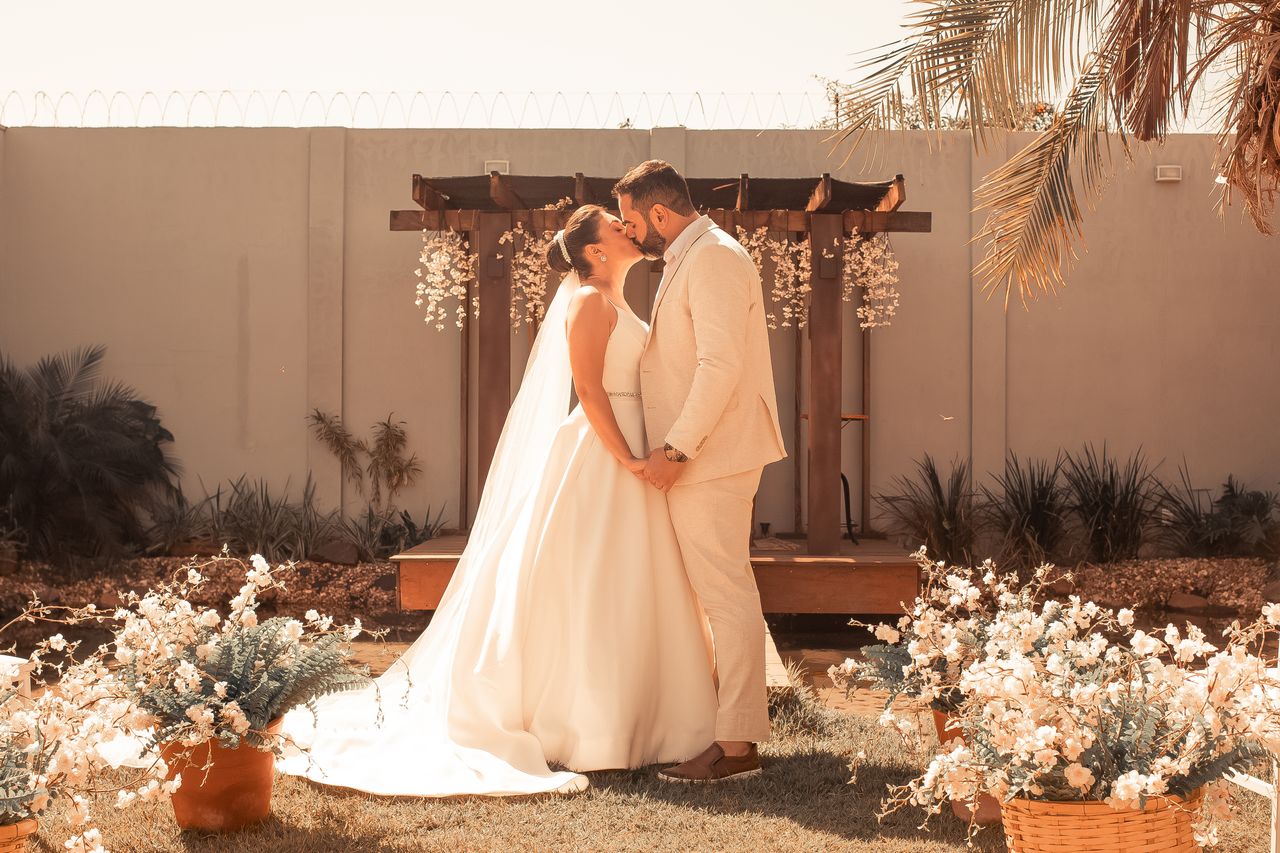 A bride and groom kissing at an outdoor summer wedding, with the groom wearing a fitted light tan suit that perfectly showcases the popular earth tone trends for groomsmen suits in Orem.