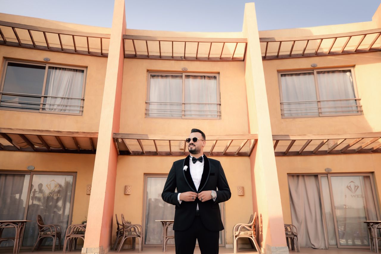 A stylish man wearing sunglasses and a classic black tuxedo with a black bow tie and distinct lapels, highlighting the elegant difference between a suit and a tuxedo.