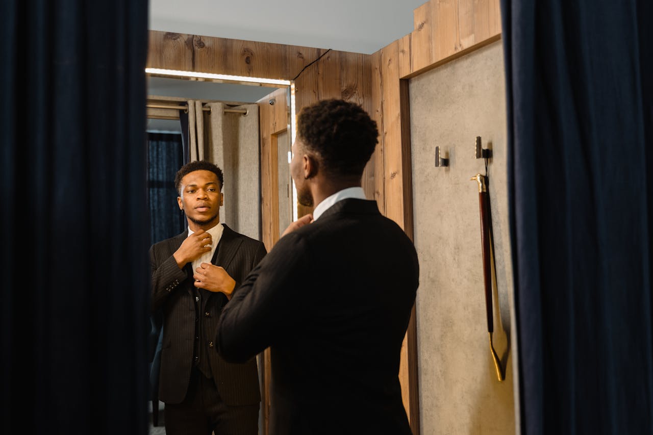 A young man admiring his perfectly fitted dark pinstripe suit in a dressing room mirror, showcasing the in-store experience when deciding to rent vs buy a suit in Orem.