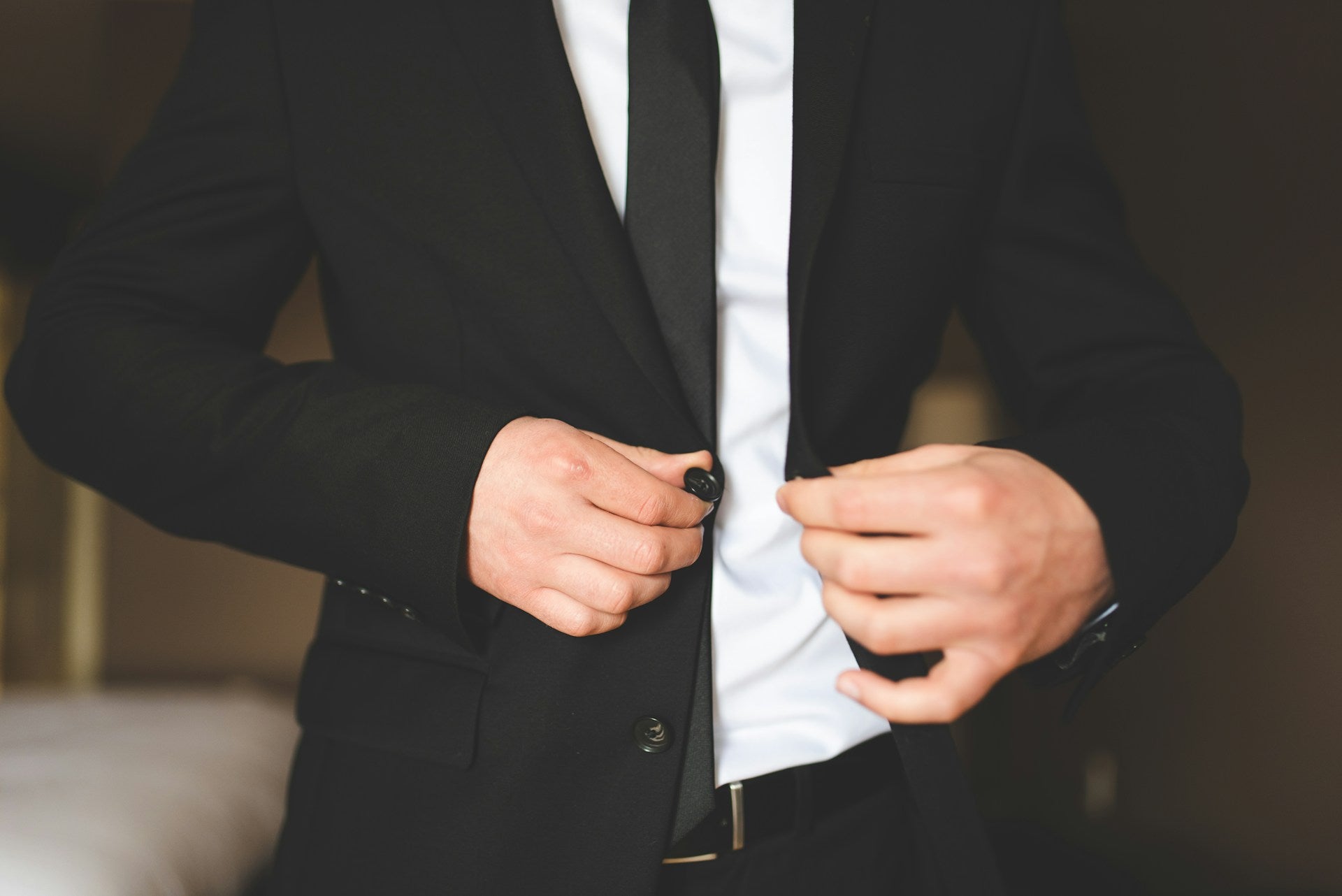Young man buttoning a tailored black jacket and classic black tie, showing the perfect fit of our missionary suits in Orem.