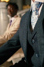 Close-up of Men's Navy Tweed Slim Fit Suit with floral tie, blurred background with man in beige suit