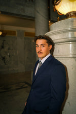 Man in Men's Navy Slim Fit Suit and tie standing in elegant marble interior with columns