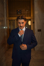 Man in a Men's Navy Slim Fit Suit adjusting tie in elegant marble hallway, formalwear for special events