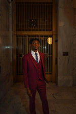 Man in Men's Burgundy Slim Fit Suit with floral tie standing in marble hallway, formalwear fashion
