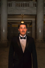 Men's black slim fit tuxedo featuring a classic two-button front with satin notch lapels and side vents for refined movement. The flat-front trousers showcase a satin side stripe and expandable waistband for comfort throughout the evening. An included dress shirt ensures you're completely outfitted for any black-tie occasion.