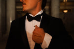Men's black slim fit tuxedo featuring a classic two-button front with satin notch lapels and side vents for refined movement. The flat-front trousers showcase a satin side stripe and expandable waistband for comfort throughout the evening. An included dress shirt ensures you're completely outfitted for any black-tie occasion.