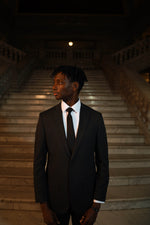 Man in Men's Black Slim Fit 2 Piece Suit with white dress shirt and black tie on plain background
