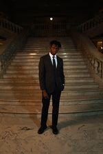 Man in Men's Black Slim Fit 2 Piece Suit with white dress shirt and black tie on plain background