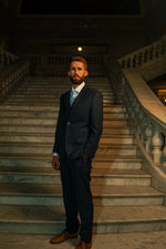 Man in a Men's Navy Tweed Slim Fit Suit and tie standing on grand marble stairs, stylish formalwear